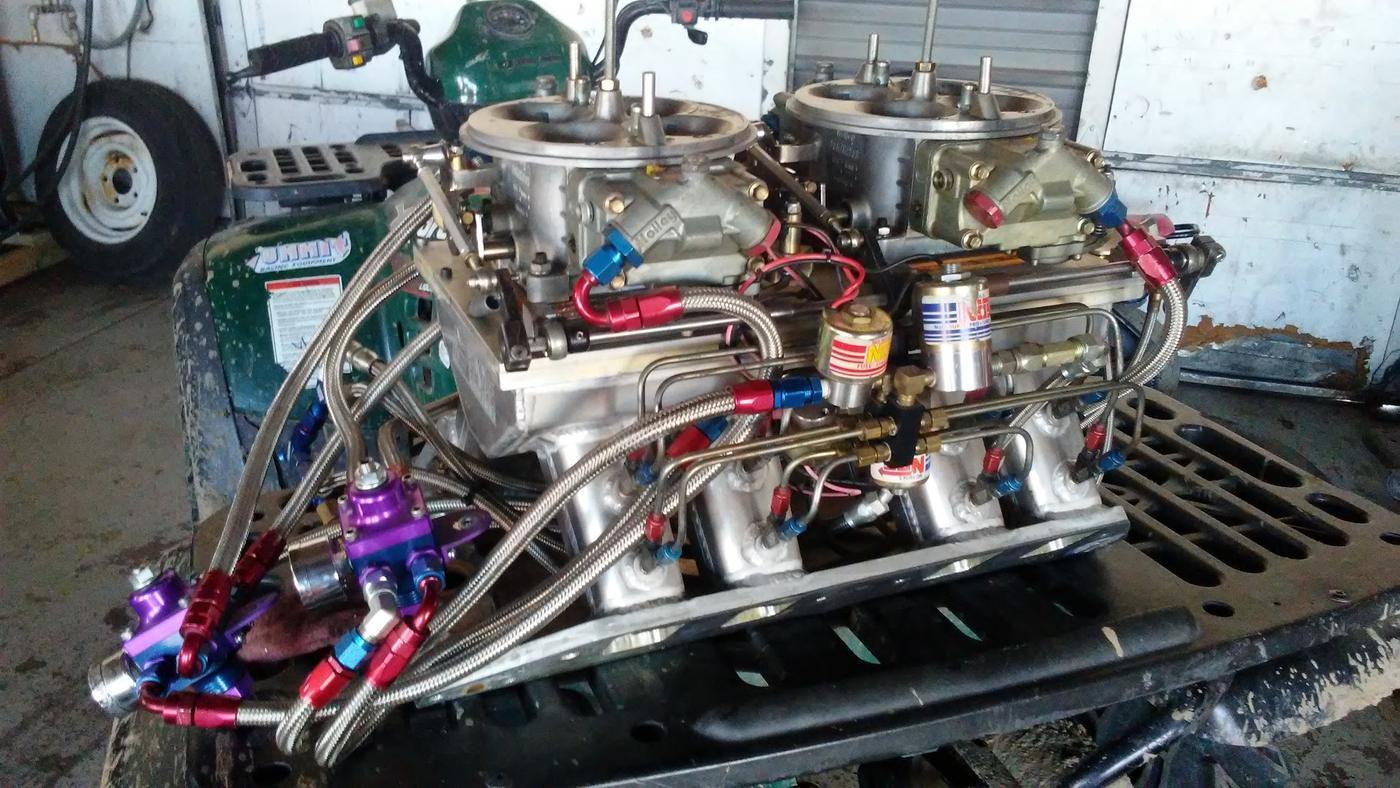 Twin carburetors on a tunnel ram intake with nitrous plumbing, photographed on the bench in the Big E's workshop